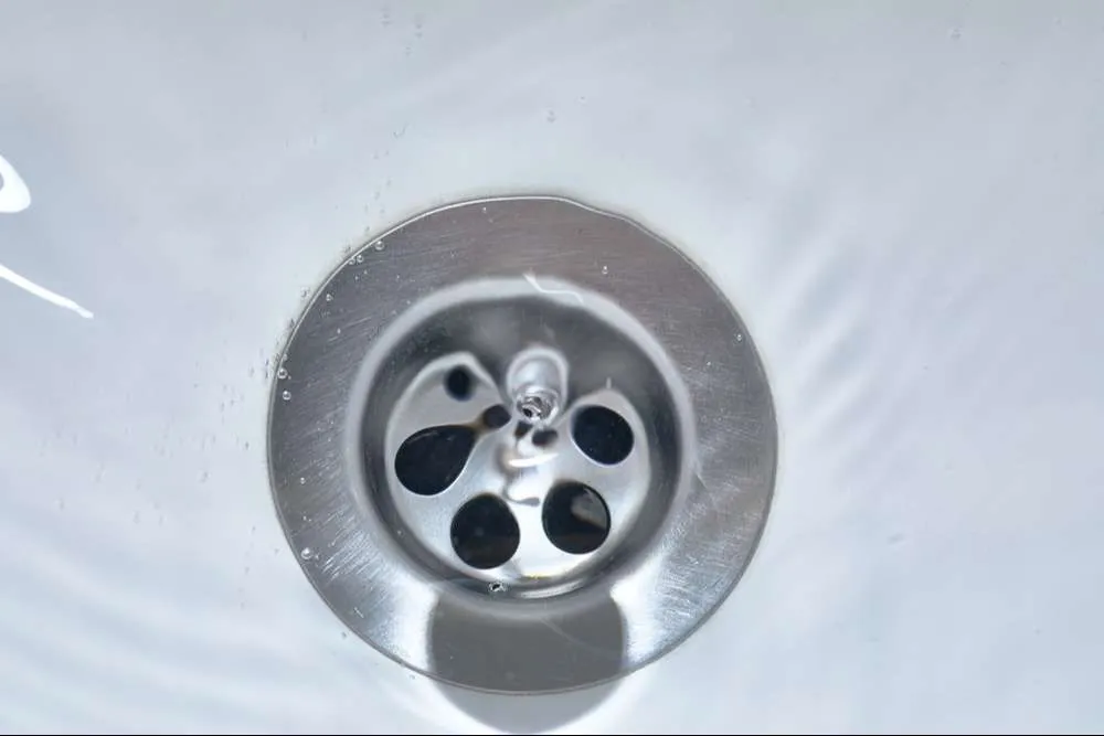 A close up of a sink drain with water running down it.